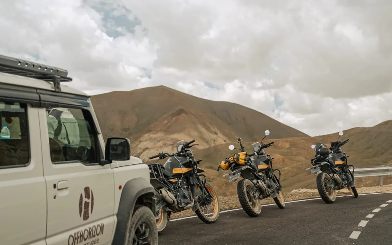 Véhicule d'assistance Offhorizon garé à côté de trois Royal Enfield Himalayan 450 sur une route de montagne