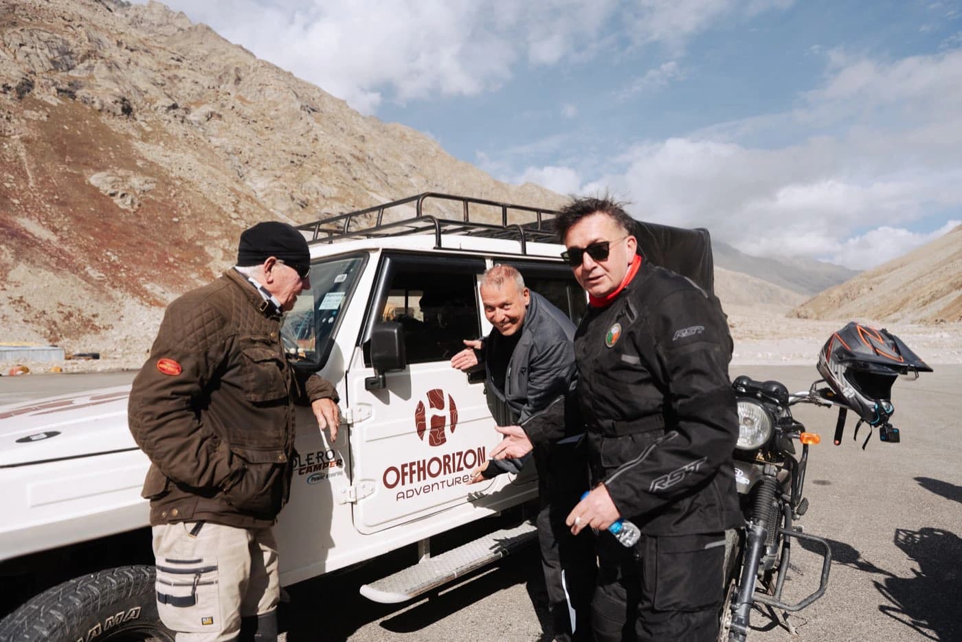 Riders joking beside the Offhorizon Adventures support vehicle before the climb to Shinku La