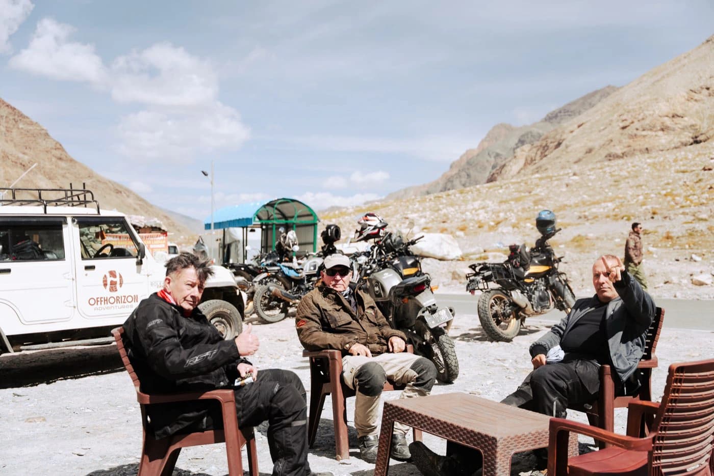 Riders resting on plastic chairs at the lunch stop in the Lungnak valley with motorcycles behind