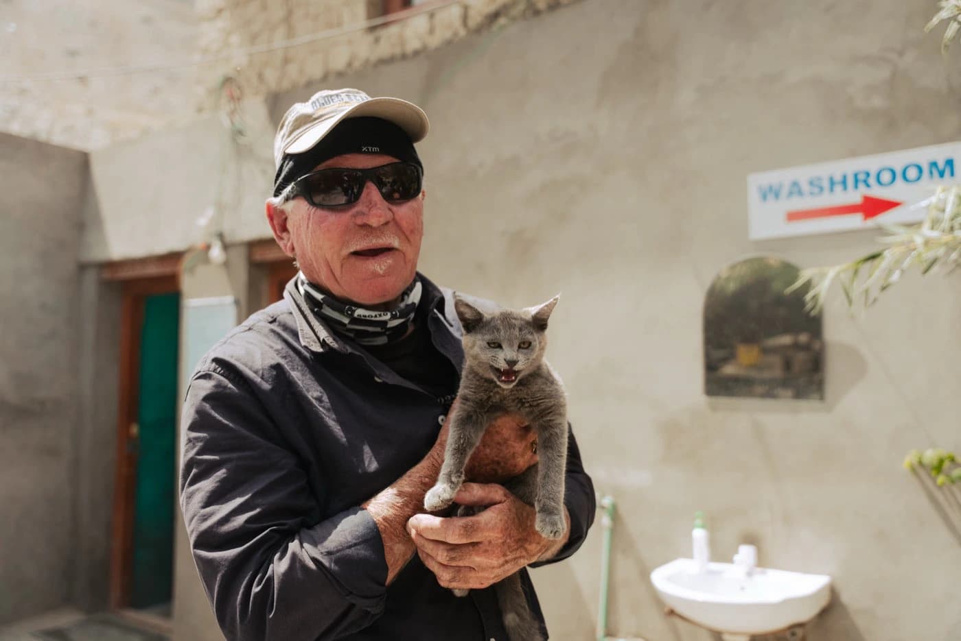 Smiling rider holding a grey kitten at a roadside stop in Zanskar