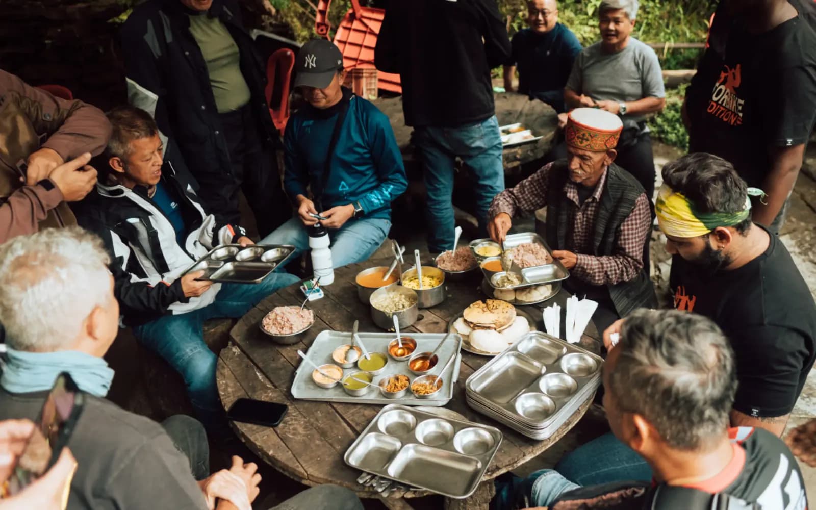 Riders and local hosts sharing a meal of local dishes served on steel plates around a wooden table