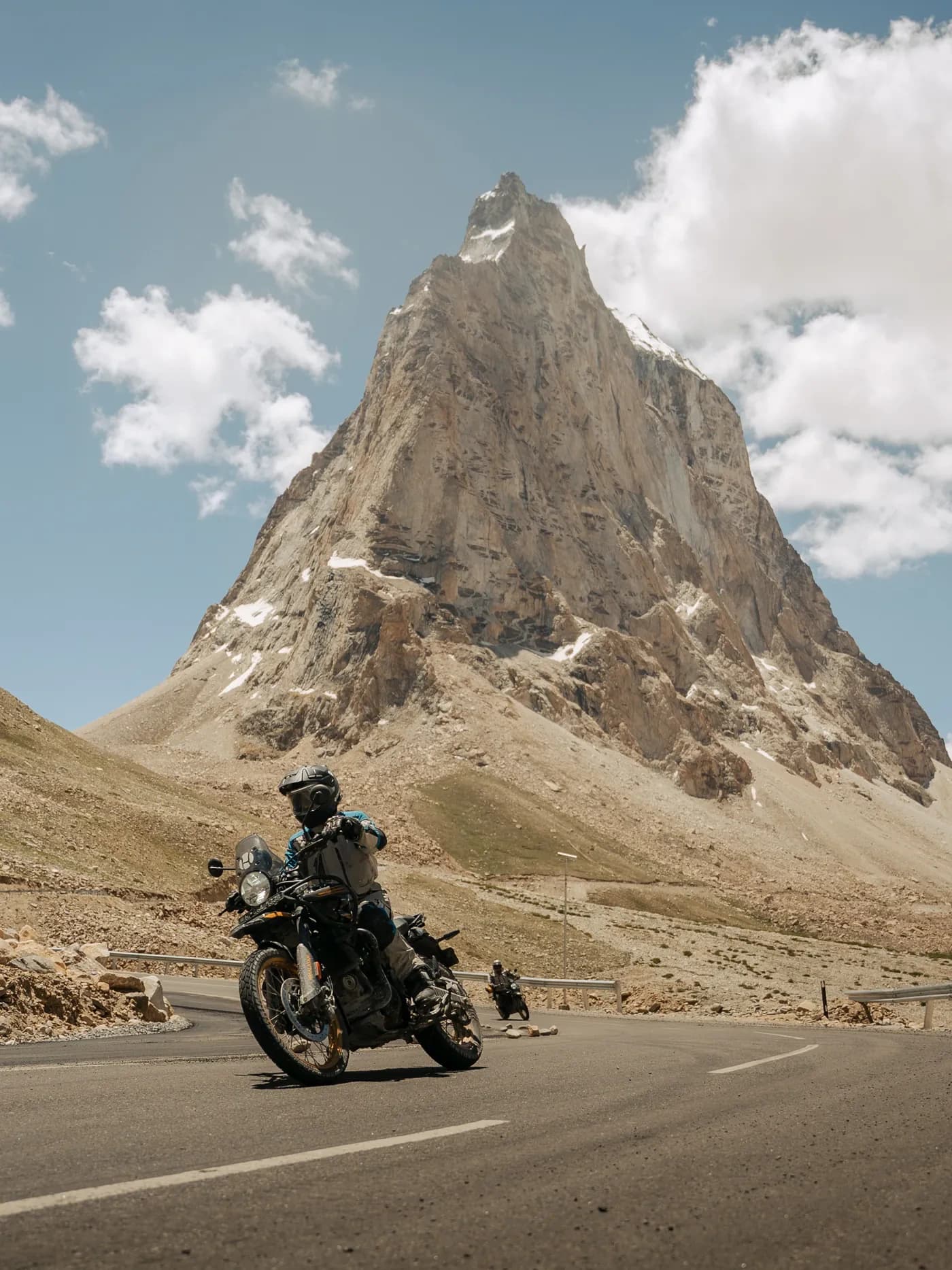 Motorcyclist riding a tarmac road beneath a sharp rocky peak