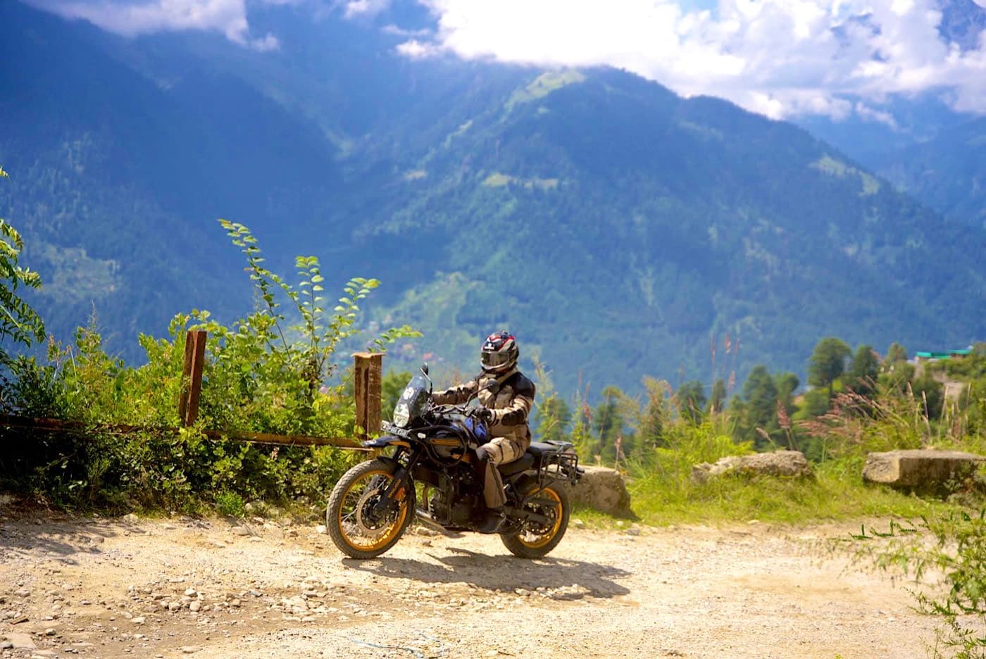 Rider on a Royal Enfield Himalayan 450 with the Kullu Valley and forested mountains behind