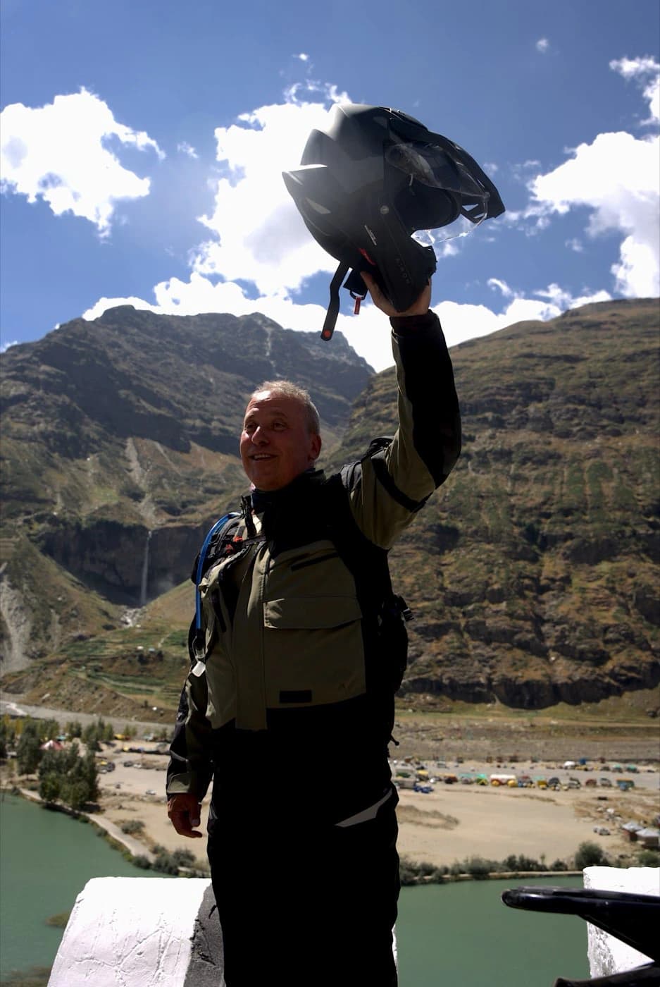 Rider waving his helmet at Sissu with the Chandra river and a waterfall behind