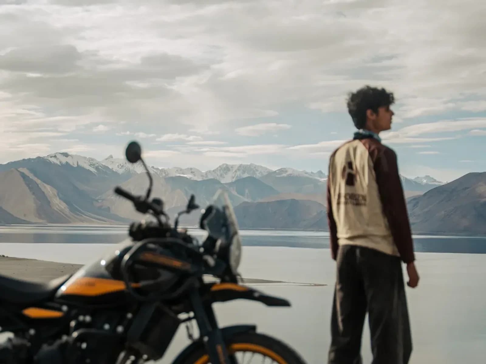 Rider beside a Royal Enfield Himalayan 450 on the shore of Pangong Tso, Ladakh