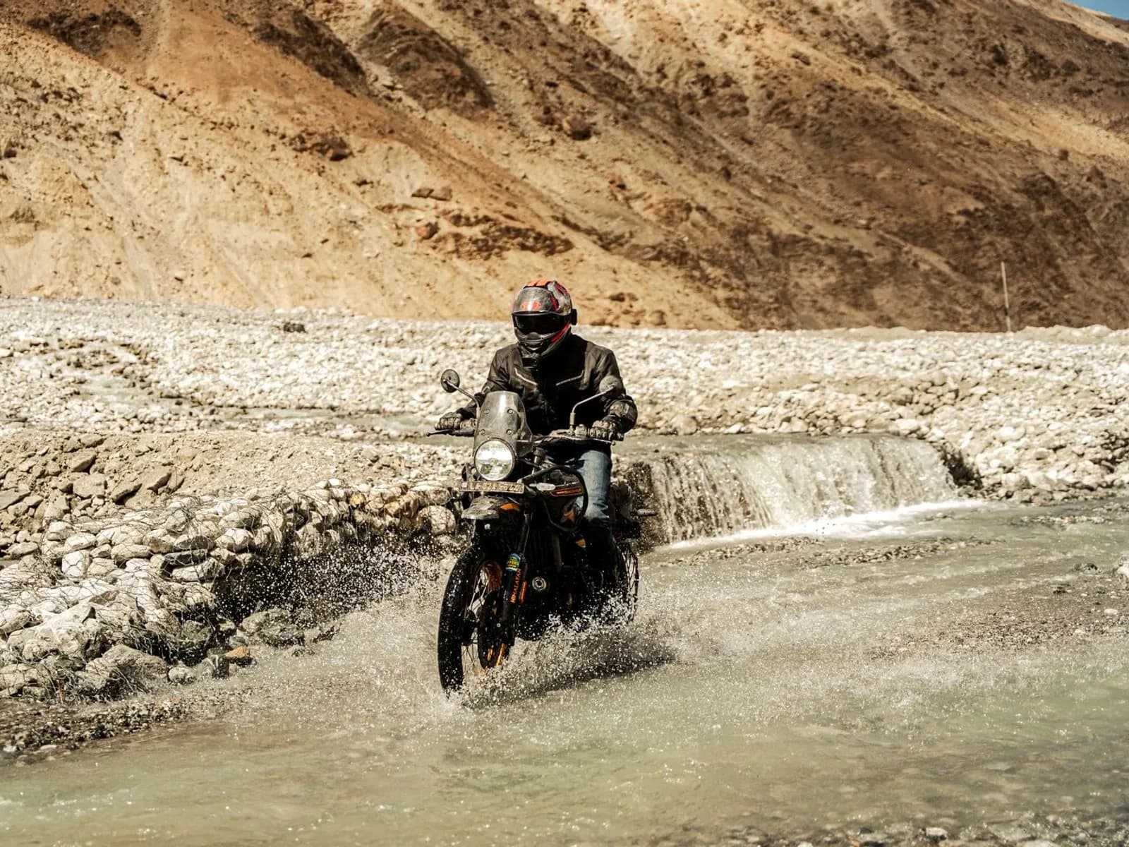 Rider splashing through a river crossing on a Royal Enfield Himalayan 450