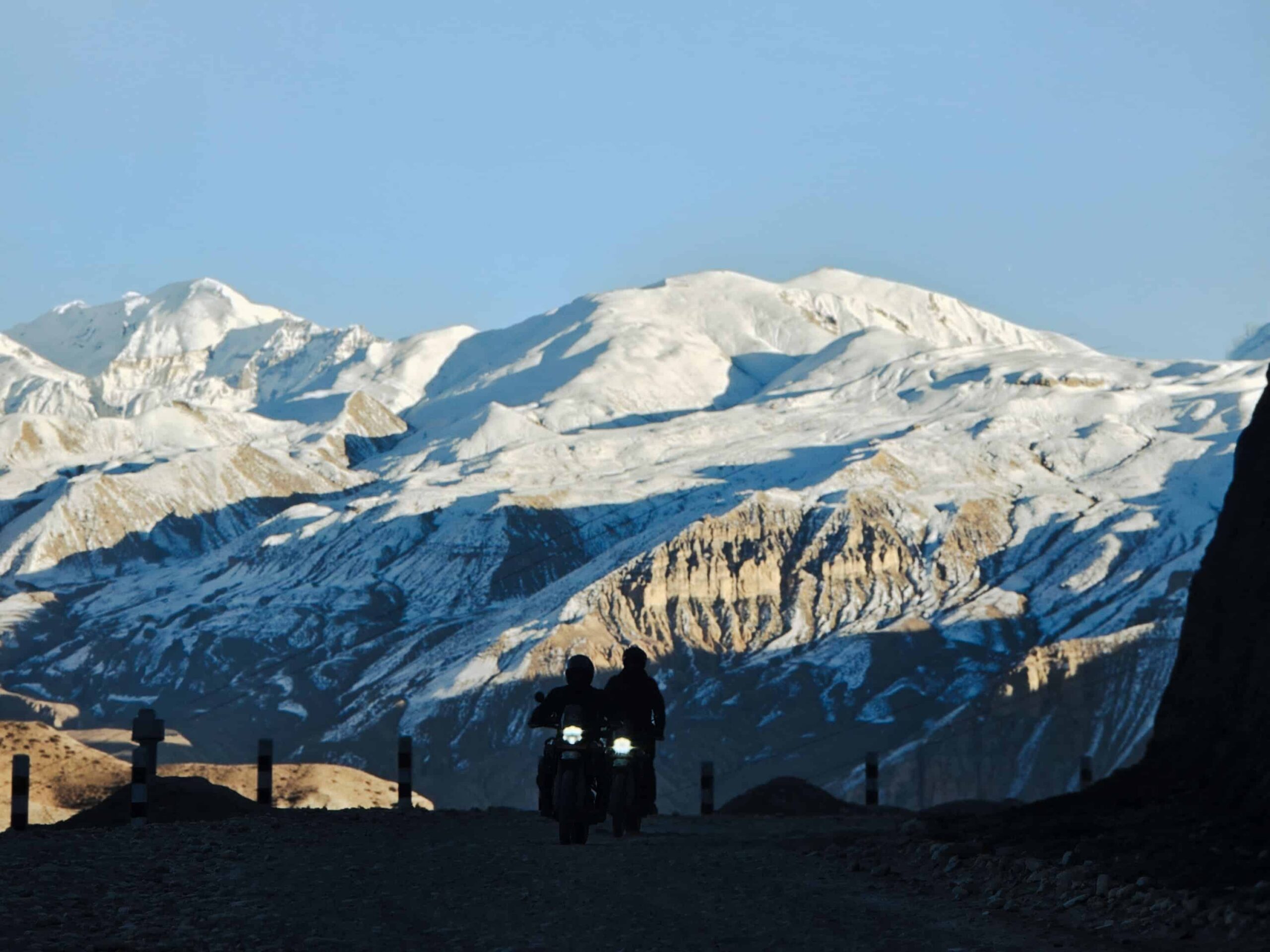 Motorcyclists riding on a remote road in Ghami Nepal with snow-covered Himalayan mountains in the background