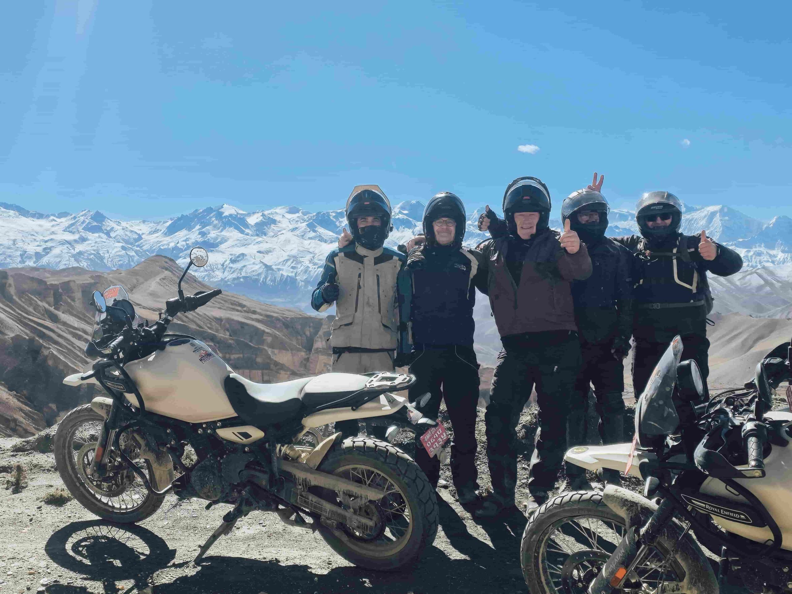 Group of motorcyclists posing with bikes on a mountain road between Ghami and Lo Manthang in Upper Mustang Nepal with Himalayan peaks in the background