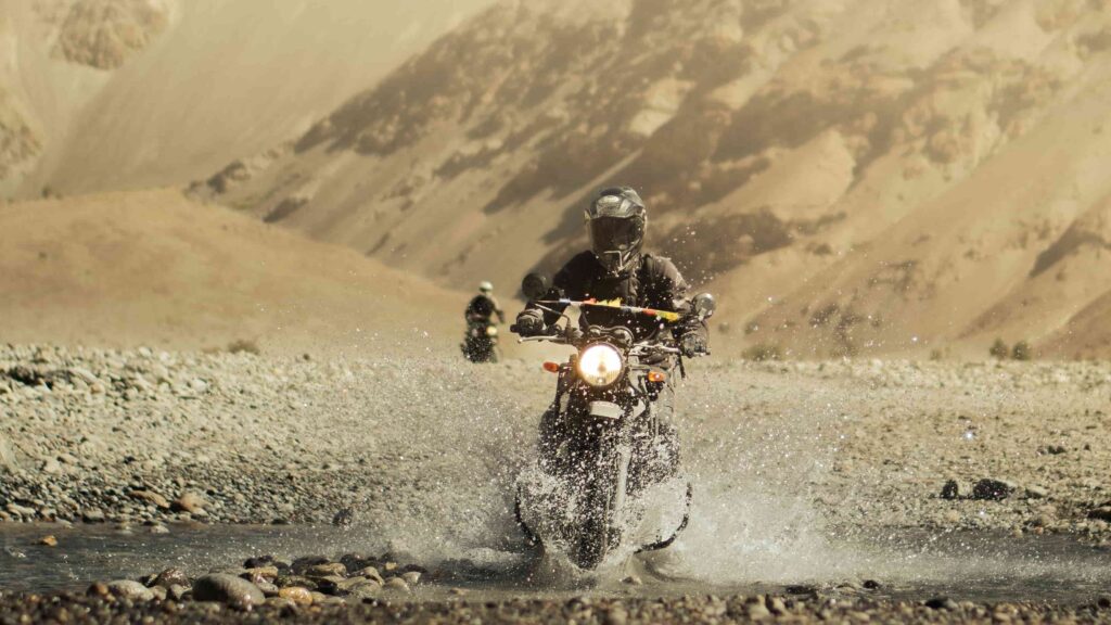 Motorcyclist riding through a river crossing during an off-road Ladakh motorcycle tour in the Himalayas.