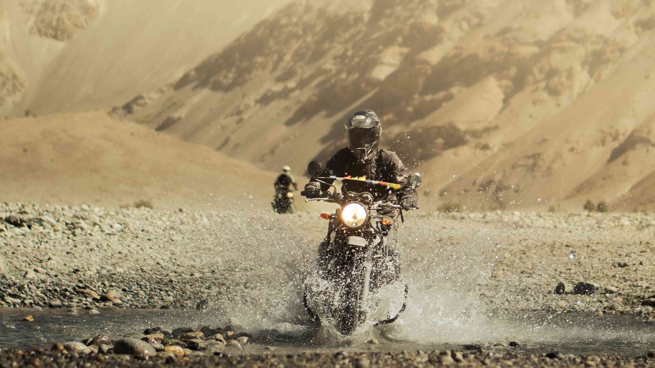 Motorcyclist riding through a river crossing during an off-road Ladakh motorcycle tour in the Himalayas.