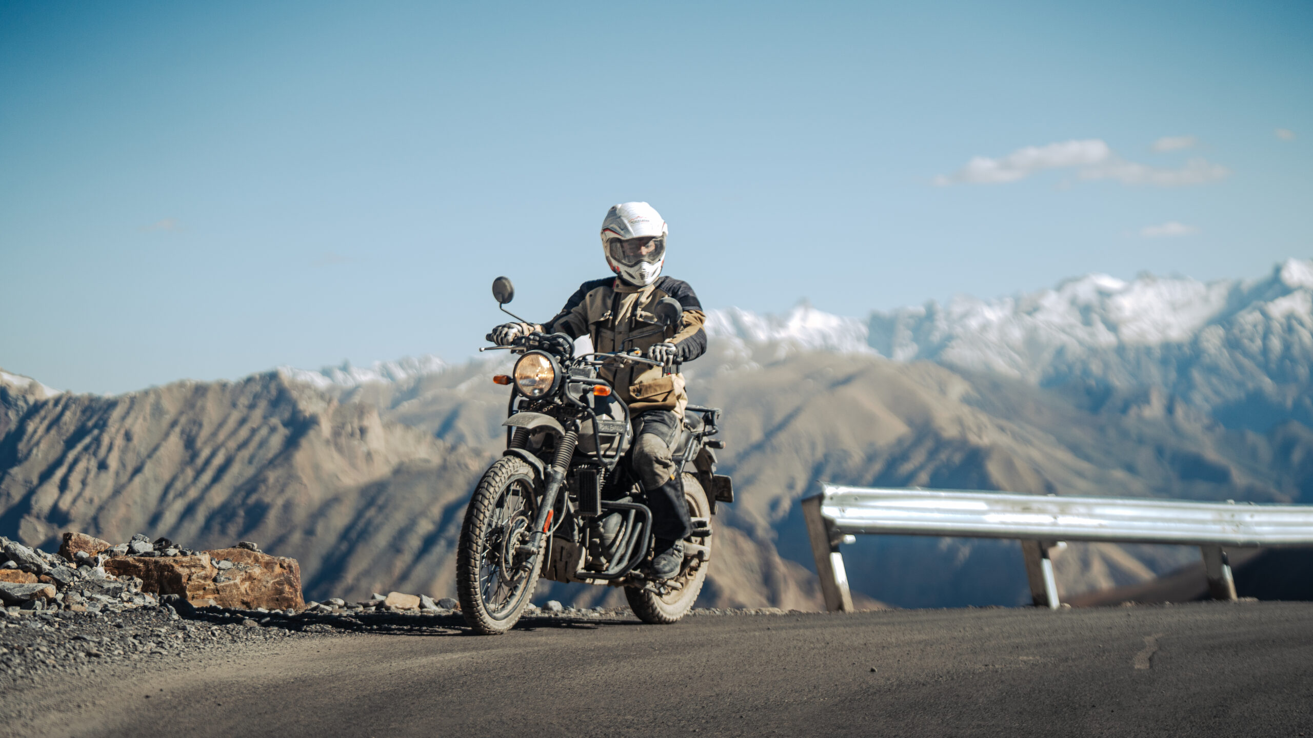 Adventure motorcyclist riding on a mountain road in the Himalayas with snow-covered peaks in the background