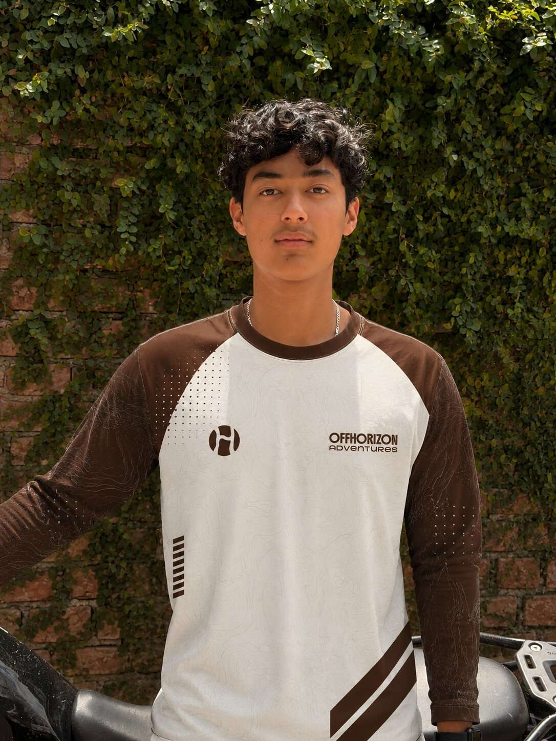 Portrait of Aditya Thakur from Offhorizon Adventures wearing branded outdoor apparel in front of a green leafy wall.