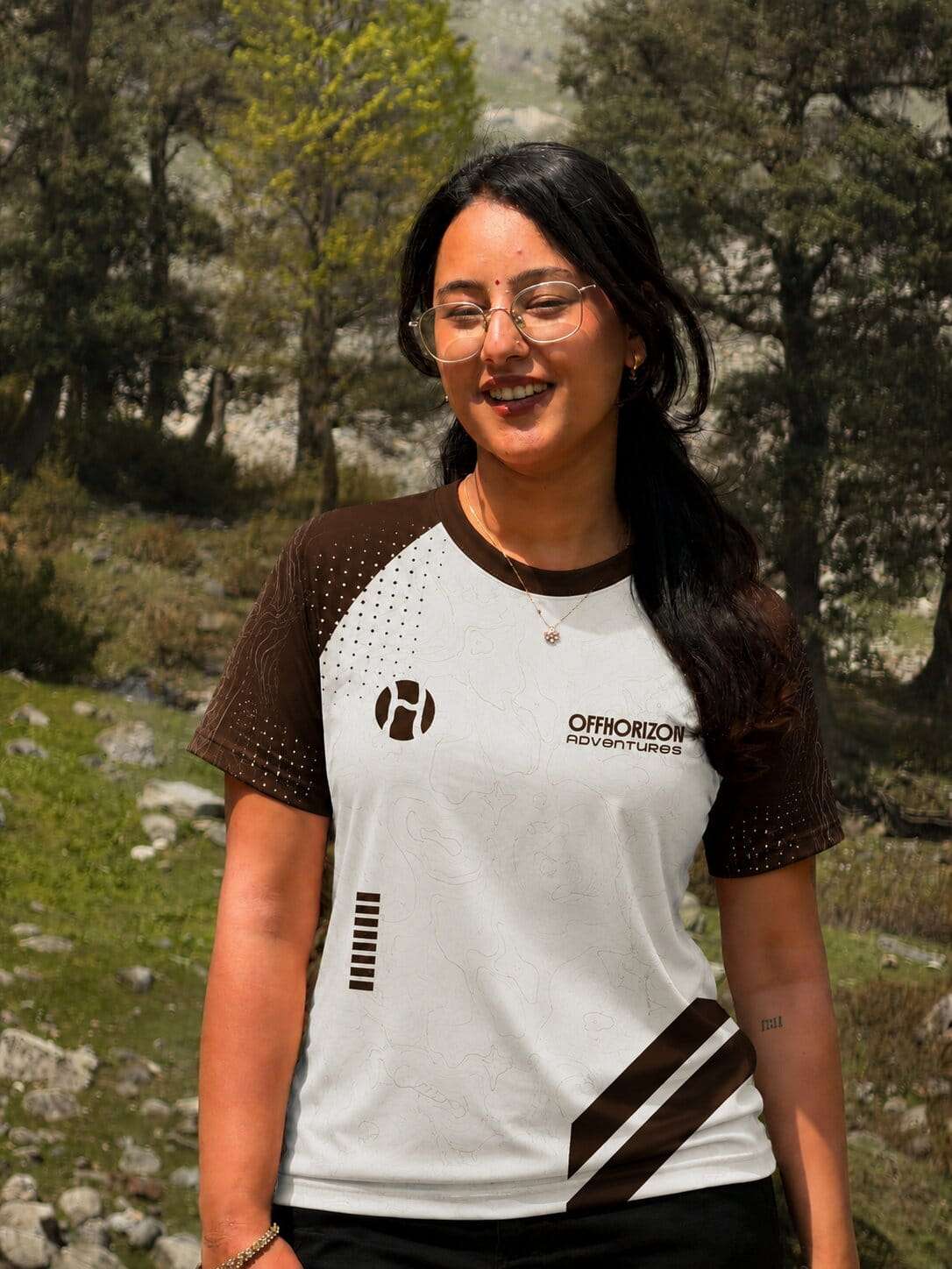 Muskan Thakur wearing an Offhorizon Adventures t-shirt while standing outdoors in a natural green landscape.
