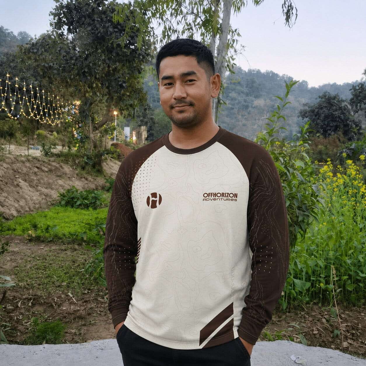 Hishe Bodh from Offhorizon Adventures standing outdoors in a green natural landscape wearing a branded adventure shirt.
