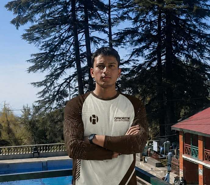Rajender Thakur from Offhorizon Adventures standing outdoors with crossed arms near pine trees and mountain scenery.