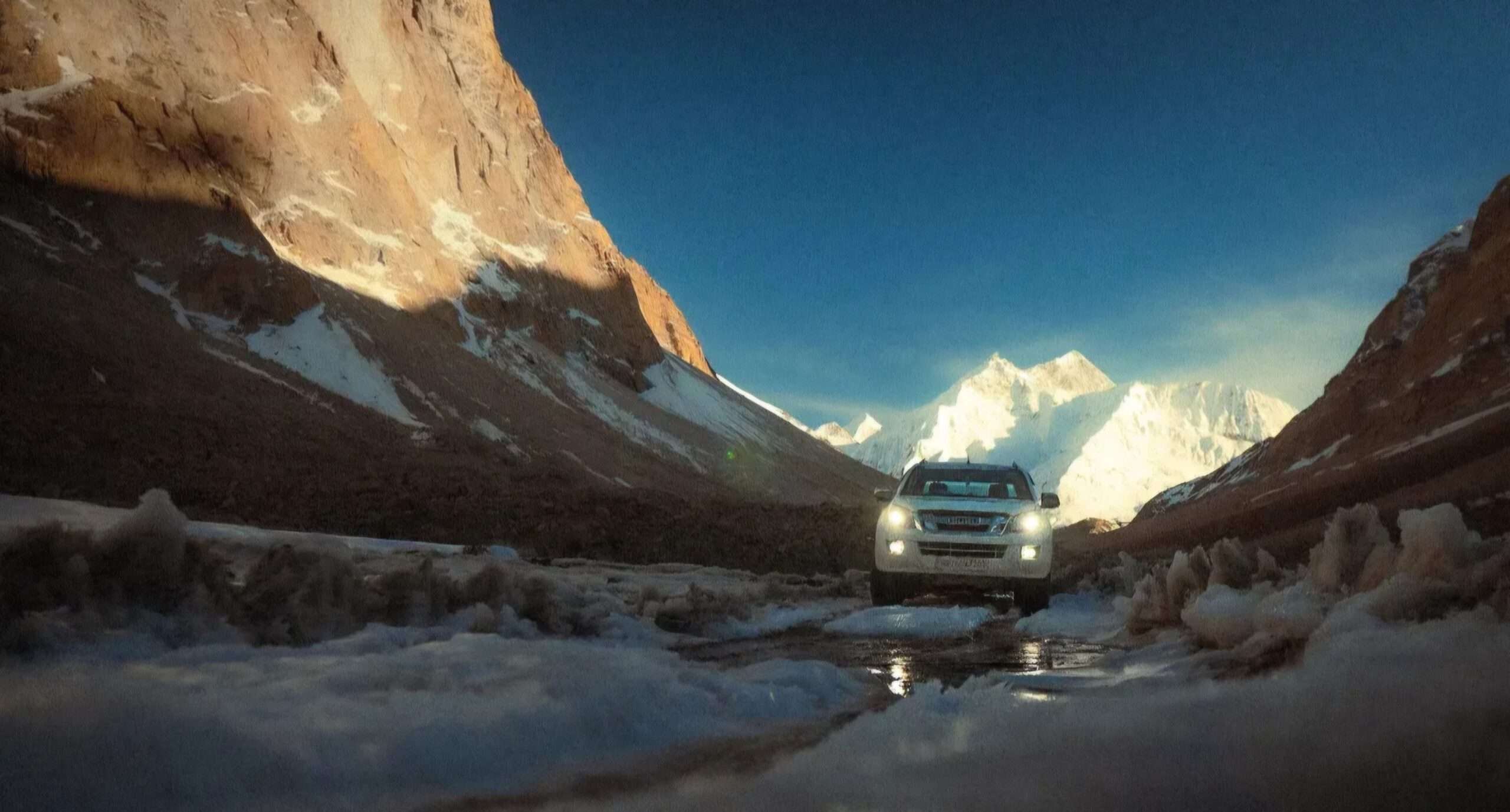 White SUV driving through a snowy valley near Kaza, Spiti Valley, surrounded by snow-capped Himalayan mountains and rugged cliffs.